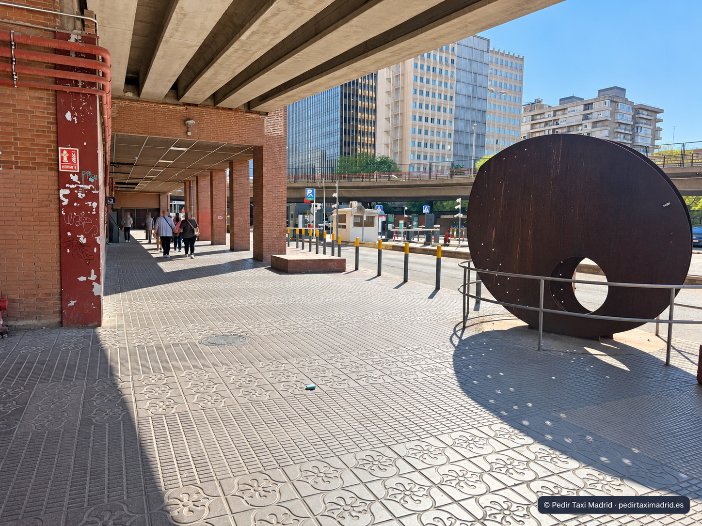 Acera exterior junto a una escultura circular negra y columnas de ladrillo
